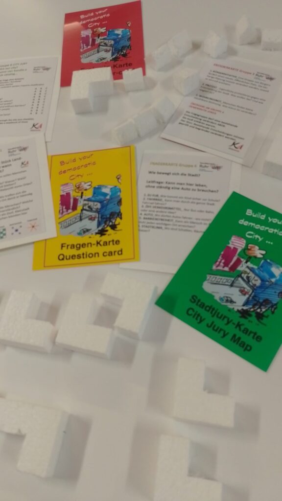 hier werden kleine Häuser und Spielkarten gezeigt, die eine Stadtentwicklung in einer Gruppe ermöglichen